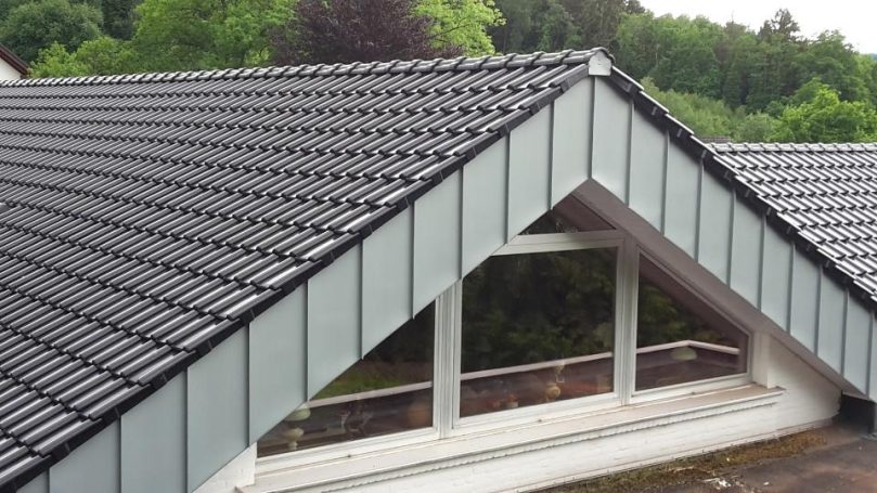 Stehpfalz Abdeckung und Ziegeleindeckung Zweiflügelige Dachkonstruktion mit schwarzen Ziegeln und großen Fenstern.
